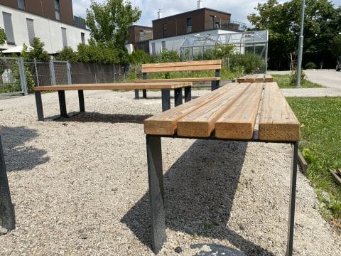 Nahaufnahme einer Sitzbank aus Holz mit Metallrahmen mit Sitzbänken im Hintergrund